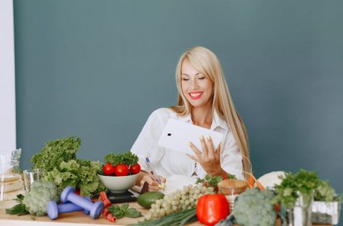 Woman using a tablet surrounded by fresh vegetables at a table, showcasing healthy lifestyle and technology.