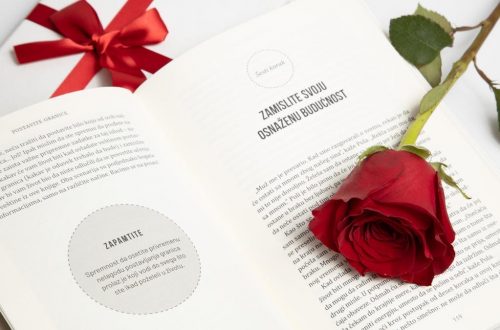 An open book with a red rose and a tied gift box next to it, conveying romance or celebration.
